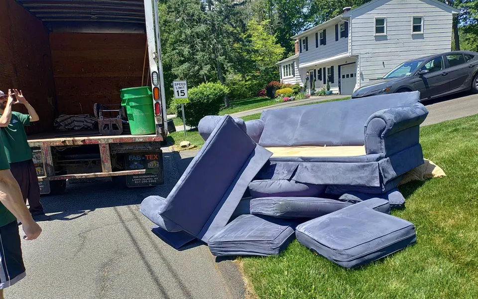 Disassembled blue sectional couch beside an open junk removal truck.